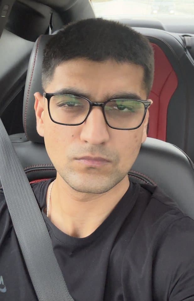Ali Asif in glasses and a black t-shirt, seated in a car